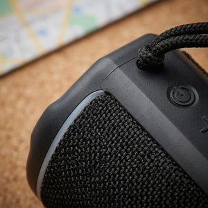 Macro detail of the Sharp GX-BT190-BK black mesh speaker, power button, and woven carry strap.