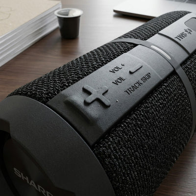 Macro detail of the Sharp GX-BT390 rugged speaker showing tactile volume controls and mesh texture.