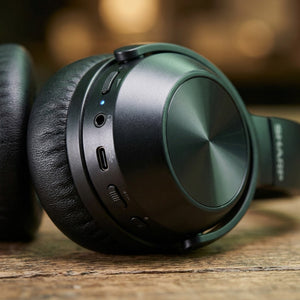 Close-up of Sharp HP-60 headphones showing USB-C port, AUX jack, and controls on a black earcup.